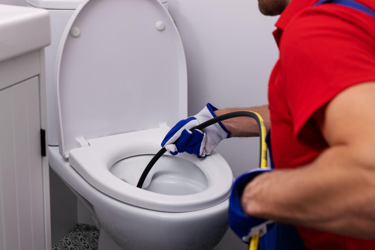 A plumber using a hydro jet machine on a home toilet.