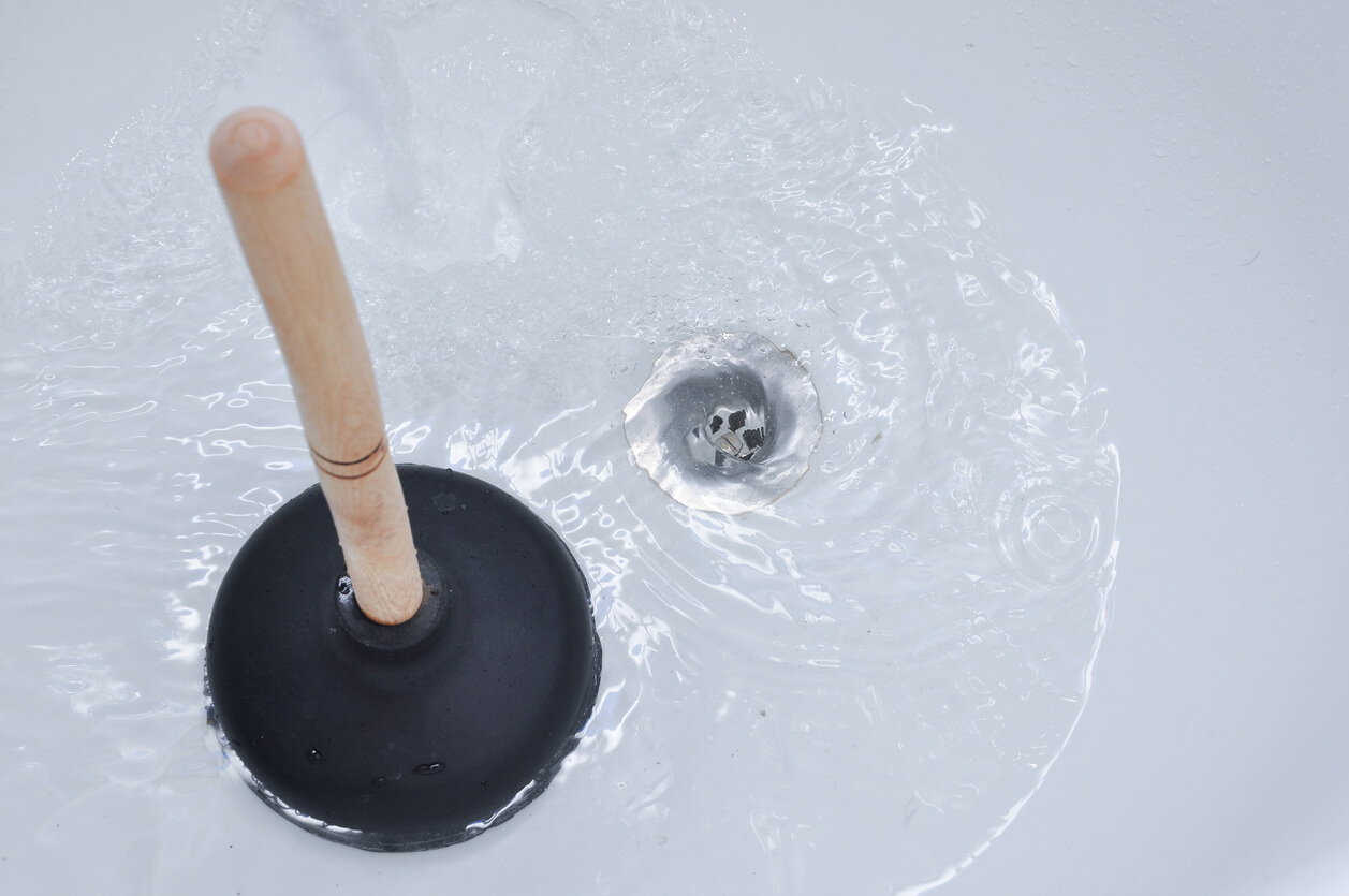 Black plunger sitting in bathtub as water runs down the cleared drain